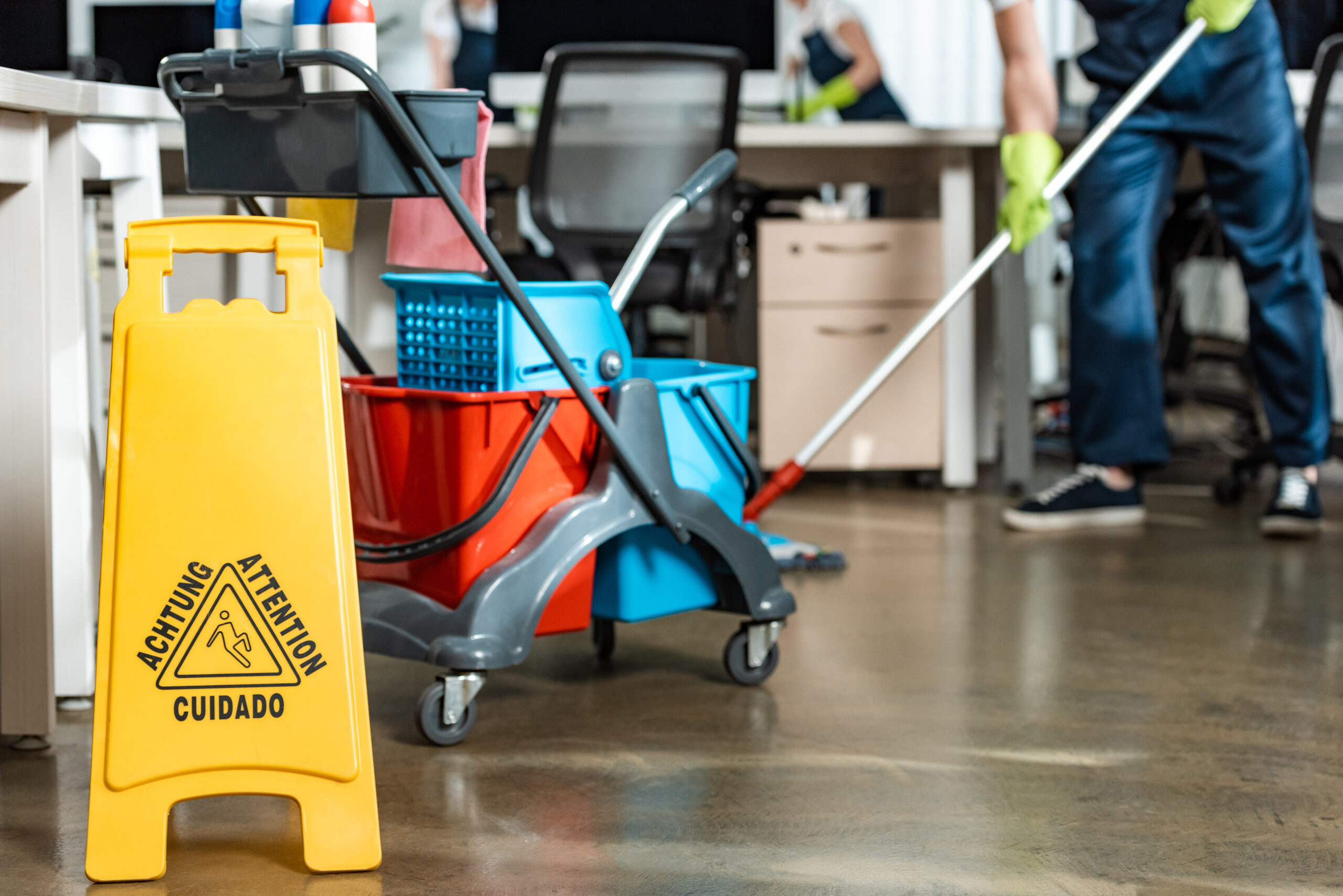 Cleaning equipment including a mop, buckets, and a caution sign in an office setting, emphasizing the importance of cleanliness and safety in schools and workplaces.