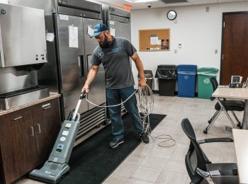 Cleaning technician using a commercial vacuum in a kitchen area, demonstrating Clean Impact LLC's commitment to exceptional service and attention to detail.