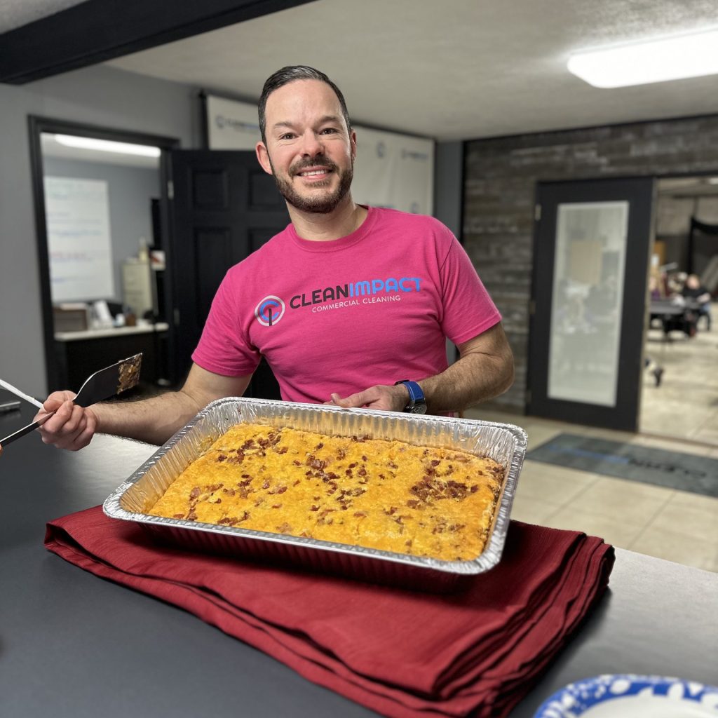 Man in a pink Clean Impact LLC shirt holding a tray of homemade food, showcasing the company's commitment to team appreciation and kindness in the workplace.